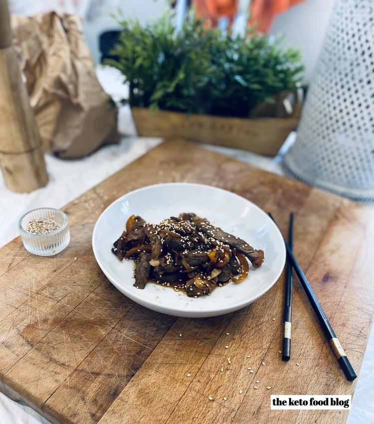 Steak stir fry with peppers and sprinkled with sesame seeds on a wooden chopping board with chopsticks