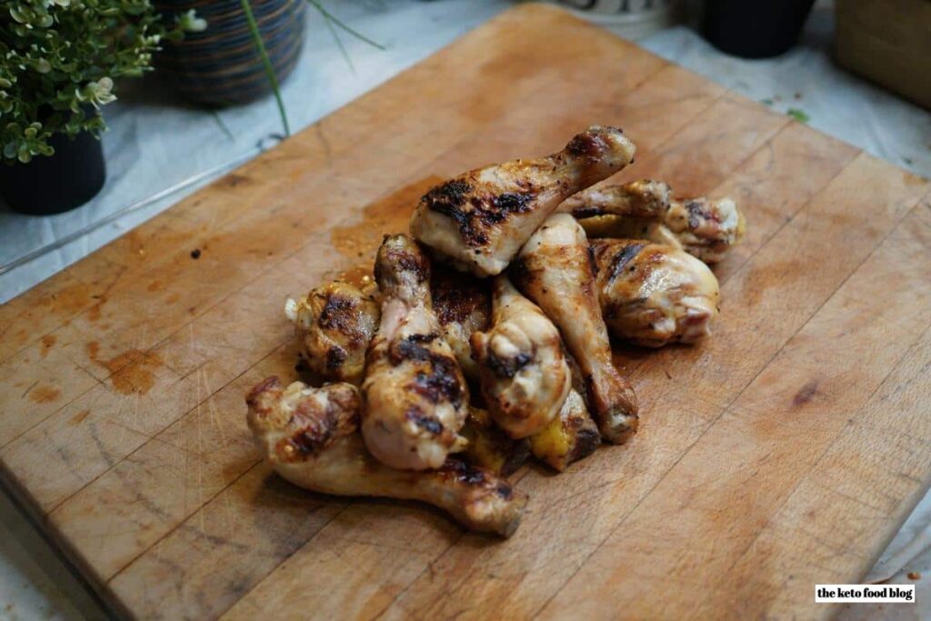 Grilled chicken drumsticks piled on a wooden chopping board