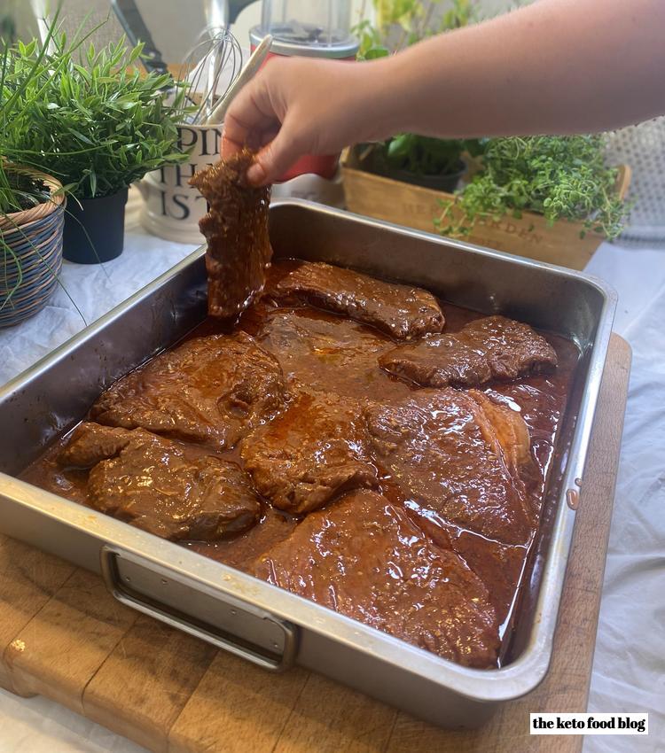 Turning over steak being marinaded in a metal roasting tin