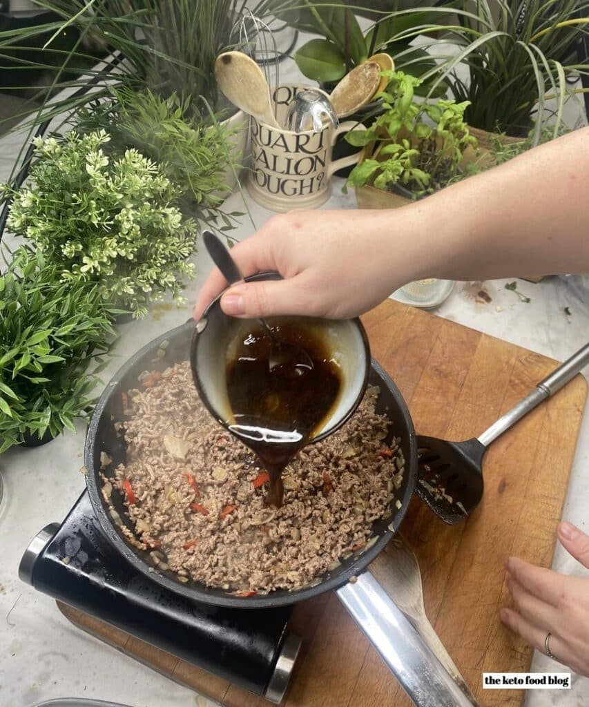 Pouring korean sauce into a pan full of ground beef