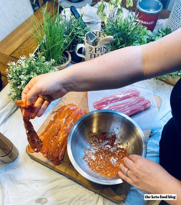 Rubbing spices into bacon strips in a metal mixing bowl