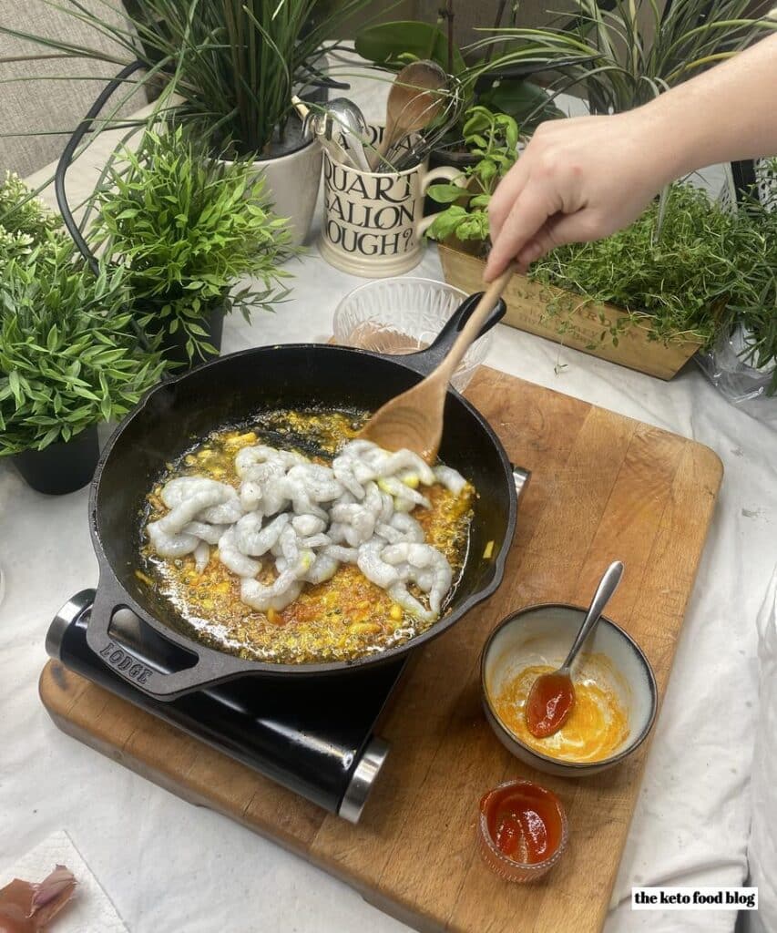 Mixing king prawns into a tumeric and saffron ensemble in a skillet