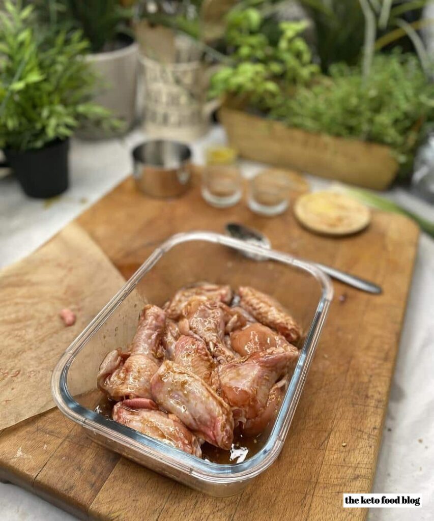 Marinading Sticky Keto Sesame Chicken Wings in a glass dish on a wooden chopping board