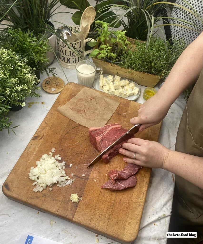 Slicing steak next to chopped onion on a chopping board