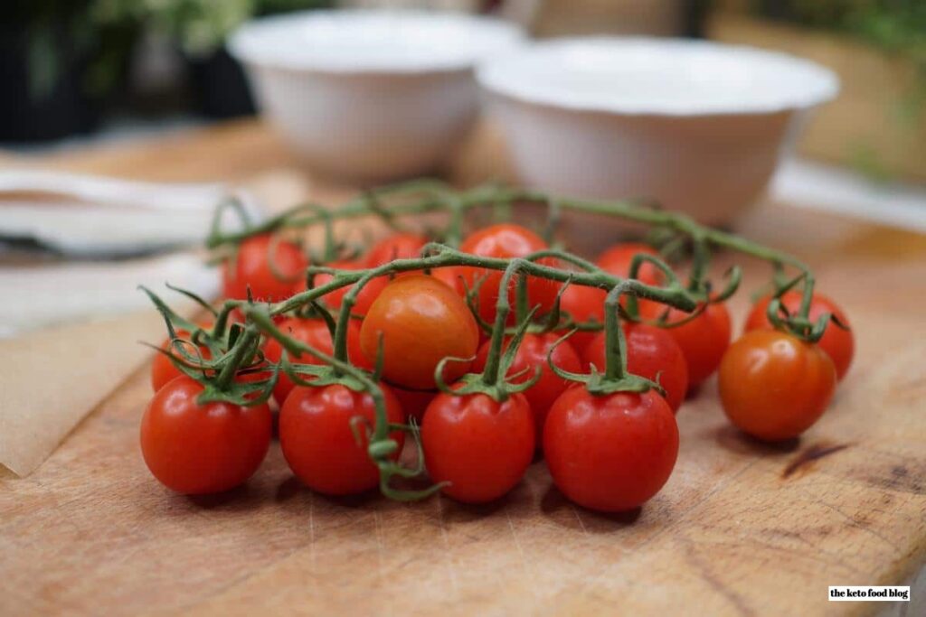 A bunch of tomatoes on a vine on a chopping board