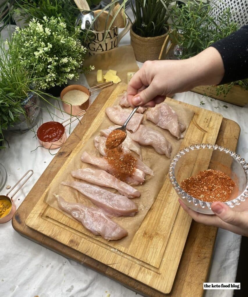 Sprinkling spice mix over the chicken strips on a wooden chopping board