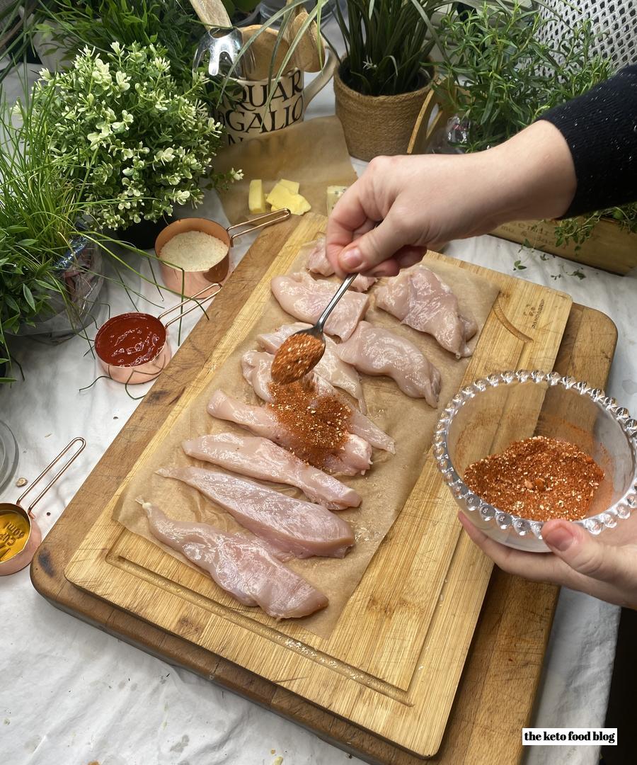 Sprinkling spice mix over the chicken on a wooden chopping board